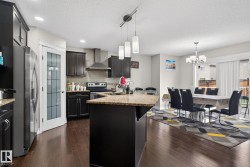 Open-concept kitchen and dining area featuring dark wood-finish flooring, a kitchen island with a stone countertop, dark cabinetry, and stainless steel appliances - 