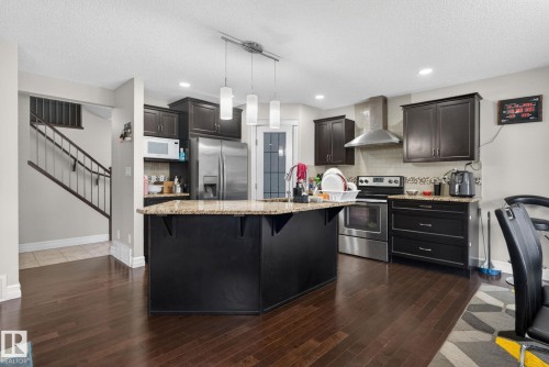 Kitchen featuring dark wood-finish cabinetry, stainless steel appliances, a center island with a light-toned countertop, and dark wood-finish flooring - 3350 18B Street, Edmonton, AB 