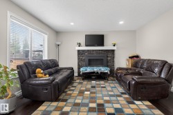 Living room featuring a stone-faced fireplace with white mantel, dark wood-finish flooring, a large window with blinds, and recessed lighting - 