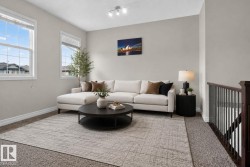 Carpeted living area featuring multiple windows with blinds, a track lighting fixture, and a wood and metal stair railing - 