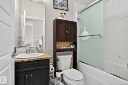Bathroom featuring a white tub with sliding frosted glass doors, a vanity with a granite-look countertop and white oval sink, dark wood-finish cabinetry, and a full-height mirror - 