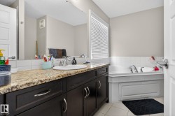 Bathroom featuring a built-in corner tub, dark wood-finish vanity with an integrated sink, granite-style countertop, and a large wall-mounted mirror - 