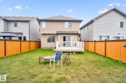 Expansive rear yard featuring a wooden privacy fence, a ground-level deck with white railings, and a beige vinyl-sided exterior - 