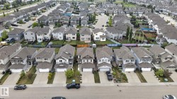Aerial perspective of a developed residential area featuring multiple detached homes with asphalt shingle roofs and integrated garages - 