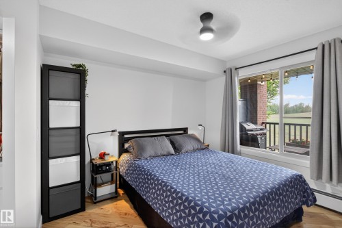 Bedroom featuring wood-finish flooring, a contemporary ceiling light fixture, and a large window - 211 3719 Whitelaw Lane, Edmonton, AB 
