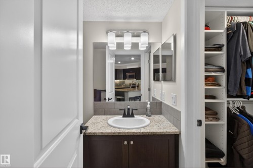 Bathroom vanity featuring a granite-style countertop, undermount sink, dark wood-finish cabinetry, and a tile backsplash - 211 3719 Whitelaw Lane, Edmonton, AB 