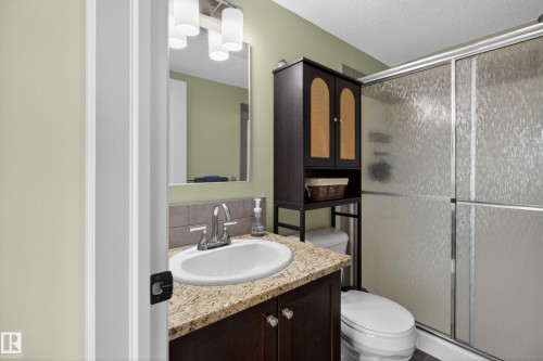 Bathroom with a vanity featuring a granite-finish countertop, a chrome faucet, and a rectangular mirror with integrated lighting - 211 3719 Whitelaw Lane, Edmonton, AB 
