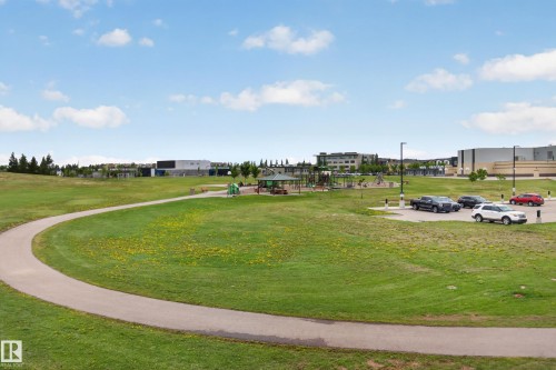 Expansive green space featuring a paved walking path, a dedicated playground area, a covered gazebo, and convenient parking facilities - 211 3719 Whitelaw Lane, Edmonton, AB 