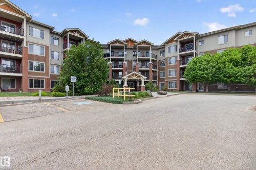 Multi-story residential building featuring a brick and siding exterior, multiple balconies with dark railings, and a covered entrance - 211 3719 Whitelaw Lane, Edmonton, AB 