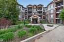 Multi-story building featuring brick and siding facade, multiple balconies with dark railings, a covered entrance, and surrounding landscaping - 211 3719 Whitelaw Lane, Edmonton, AB 