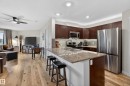 Gourmet kitchen with rich wood cabinetry, stainless steel appliances, and a spacious island featuring stone countertops and integrated sink - 211 3719 Whitelaw Lane, Edmonton, AB 