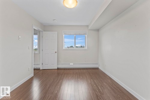 Bedroom featuring wood-finish flooring, a window with outdoor scenery, baseboard heating, a ceiling-mounted light fixture, and white trim - 1302-1601 8 Avenue, Cold Lake, AB 