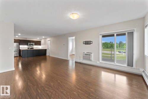 Spacious living area featuring wood-finish flooring, a sliding glass door to an exterior balcony, and a dedicated kitchen space with dark cabinetry and stainless steel appliances - 1302-1601 8 Avenue, Cold Lake, AB 
