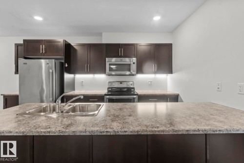 Kitchen featuring dark wood-finish cabinetry, stainless steel appliances, and light-toned countertops - 1302-1601 8 Avenue, Cold Lake, AB 