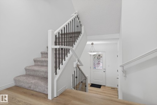 Multi-level entryway featuring wood-finish flooring and a carpeted staircase with white risers - 3806 Powell Wynd, Edmonton, AB 