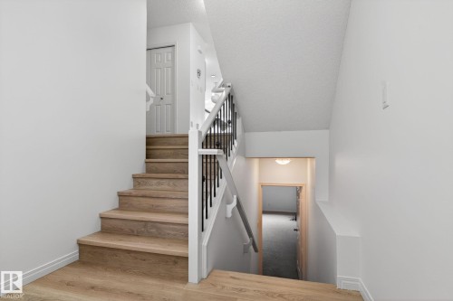 Staircase featuring wood-finish treads and risers, white painted walls, and a white handrail with black metal spindles - 3806 Powell Wynd, Edmonton, AB 