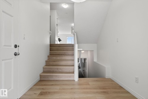 Inviting entryway featuring light wood-finish flooring, a paneled entry door with chrome hardware, and a staircase with matching wood-finish treads - 3806 Powell Wynd, Edmonton, AB 