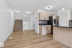 Open-concept living space featuring wood-finish flooring, a contemporary kitchen with light wood-finish cabinetry, dark countertops, and a mosaic tile backsplash - 