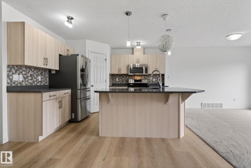 Modern kitchen featuring light wood-finish cabinetry, dark countertops, and a patterned tile backsplash - 3806 Powell Wynd, Edmonton, AB 