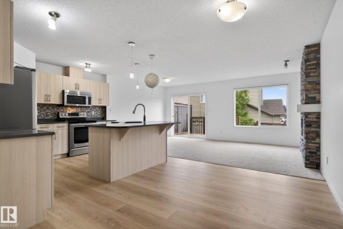 Open concept living space featuring wood-finish flooring in the kitchen, a central island with a dark countertop and sink, and stainless steel appliances - 3806 Powell Wynd, Edmonton, AB 