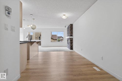 Wood-finish flooring extending into a spacious living area with a stone-clad fireplace and a white mantel - 3806 Powell Wynd, Edmonton, AB 