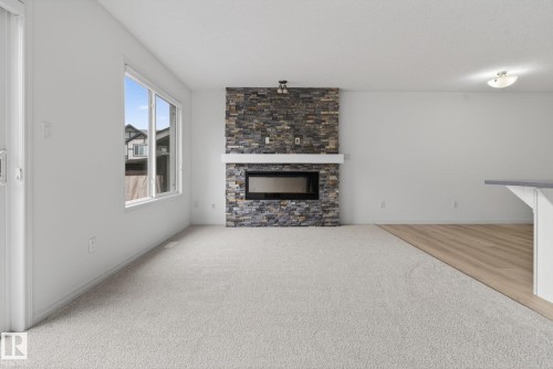 Living area featuring a floor-to-ceiling stone-faced fireplace with a contemporary electric insert and a white mantle - 3806 Powell Wynd, Edmonton, AB 