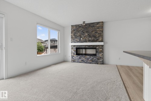 Living space featuring a stacked stone fireplace with a contemporary linear insert and a white mantel - 3806 Powell Wynd, Edmonton, AB 