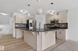 Kitchen featuring a central island with a dark countertop, light wood-finish cabinetry, a mosaic tile backsplash, and stainless steel appliances - 
