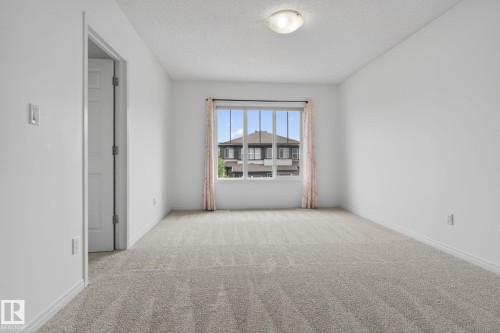 Carpeted room featuring a large window, neutral wall paint, and a flush-mount ceiling light fixture - 3806 Powell Wynd, Edmonton, AB 