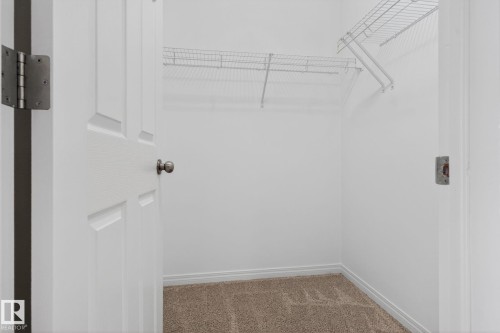 Interior closet with white wire shelving, light brown carpeting, white baseboards, and a paneled white door with a round dark-toned doorknob - 3806 Powell Wynd, Edmonton, AB 