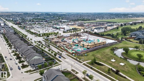Aerial overview showcasing a developed residential area with row homes, commercial properties, and a golf course - 3806 Powell Wynd, Edmonton, AB 