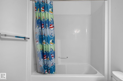 White fiberglass tub and shower combination with an integrated grab bar and chrome towel bar - 3806 Powell Wynd, Edmonton, AB 