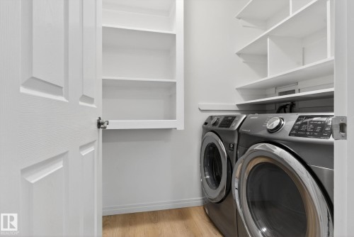 Dedicated laundry space featuring a front-loading washer and dryer, extensive white shelving, and wood-finish flooring - 3806 Powell Wynd, Edmonton, AB 