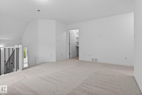 Spacious carpeted room featuring a neutral color palette, white walls, white trim, and an open doorway leading to a closet with built-in shelving - 3806 Powell Wynd, Edmonton, AB 
