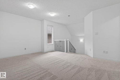 Carpeted open area featuring a window, overhead lighting, an angled ceiling, and a staircase with a black metal railing - 3806 Powell Wynd, Edmonton, AB 