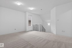 Carpeted open area featuring a window, overhead lighting, an angled ceiling, and a staircase with a black metal railing - 
