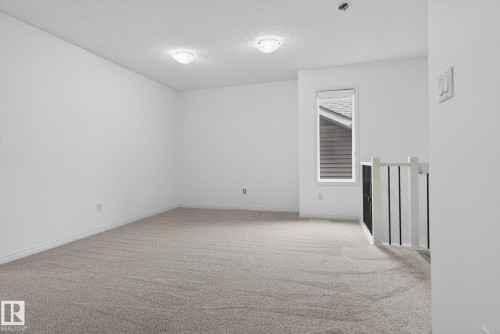 Carpeted room featuring white walls, a single window, and a white and black spindle railing - 3806 Powell Wynd, Edmonton, AB 