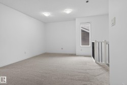 Carpeted room featuring white walls, a single window, and a white and black spindle railing - 