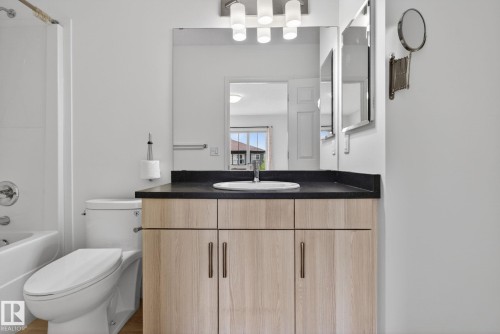 Bathroom featuring a light wood-finish vanity with a dark countertop, an undermount sink, and a modern light fixture - 3806 Powell Wynd, Edmonton, AB 
