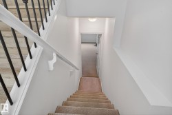 Staircase featuring carpeted treads, a white handrail, and black metal balusters - 