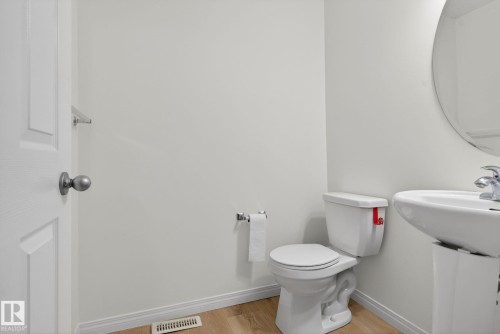 Compact bathroom featuring a white pedestal sink with chrome fixtures, a round wall-mounted mirror, and a white toilet - 3806 Powell Wynd, Edmonton, AB 