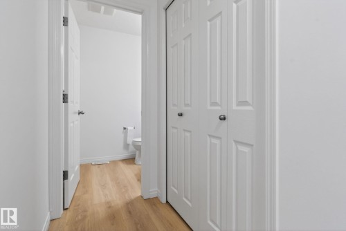 Hallway with wood-finish flooring, white walls, and white bi-fold closet doors - 3806 Powell Wynd, Edmonton, AB 