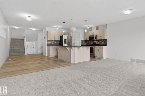 Open-concept living space featuring a kitchen with light-finish cabinetry, stainless steel appliances, and a dark-finish countertop with an integrated sink - 3806 Powell Wynd, Edmonton, AB 