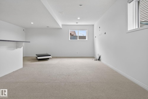 Spacious lower-level room featuring light-colored carpeting, white walls, two windows, and recessed ceiling lighting - 3806 Powell Wynd, Edmonton, AB 