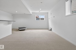 Spacious lower-level room featuring light-colored carpeting, white walls, two windows, and recessed ceiling lighting - 