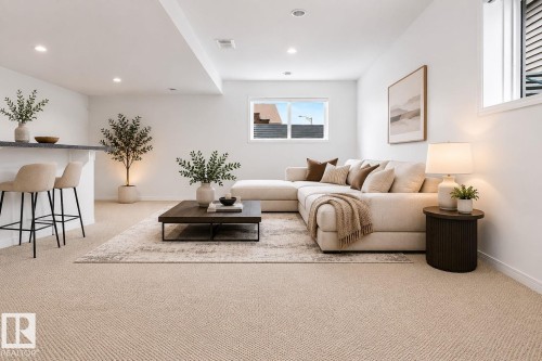 Open-concept living area featuring light-toned carpeting, a built-in bar with a dark countertop, recessed lighting, and a large window providing natural illumination - 3806 Powell Wynd, Edmonton, AB 