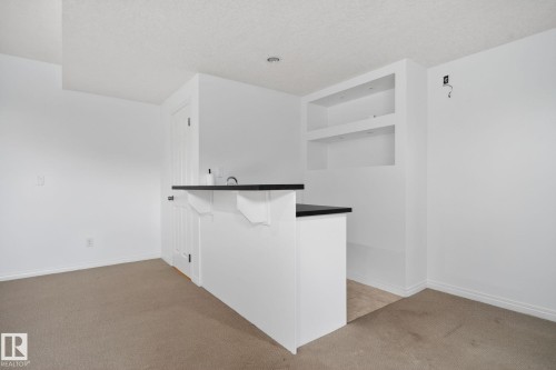 Built-in bar with a dark countertop and integrated sink, complemented by recessed shelving with accent lighting - 3806 Powell Wynd, Edmonton, AB 