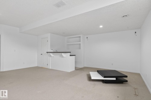 Finished basement room featuring a built-in bar with a dark countertop and white cabinetry, recessed lighting, and wall-mounted shelving - 3806 Powell Wynd, Edmonton, AB 