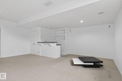 Finished basement room featuring a built-in bar with a dark countertop and white cabinetry, recessed lighting, and wall-mounted shelving - 