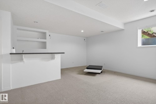 Finished basement space featuring a built-in bar with dark countertop and integrated shelving - 3806 Powell Wynd, Edmonton, AB 